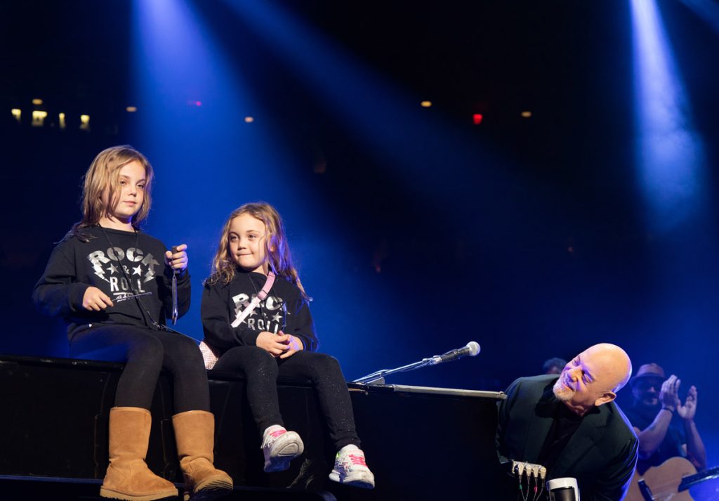 Billy Joel with daughters Della Rose Joel and Remy Anne Joel sitting on his piano during his concert at Madison Square Garden New York, NY on October 20, 2023